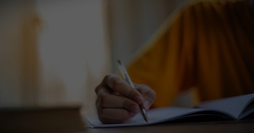 Close-up of a person writing in a notebook with a pen.