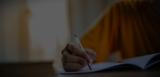 Close-up of a person writing in a notebook with a pen.
