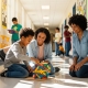 Teachers assisting a student with a hands-on classroom activity in a school hallway.