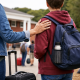 Parent placing a reassuring hand on a teenager’s shoulder during boarding school drop-off, with luggage and campus buildings in the background